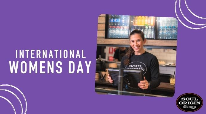 Team member at POS till with a purple background and “International Women’s Day” in writing